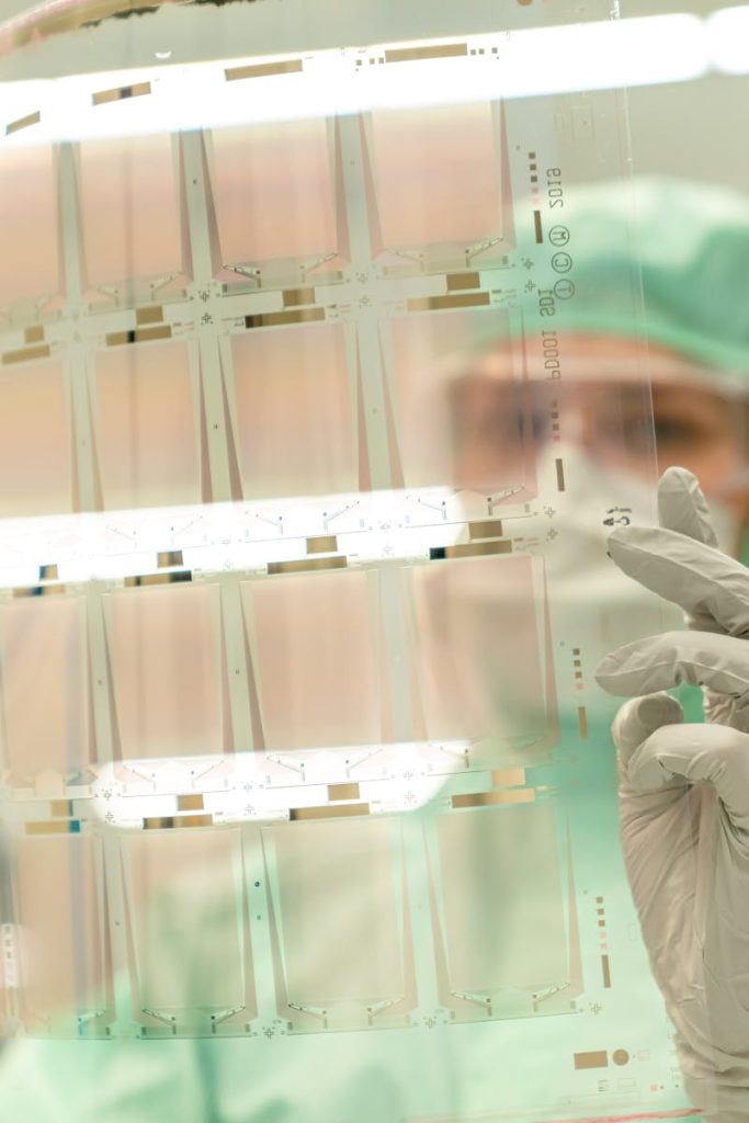 Scientist in protective gear holding a transparent test sheet in a laboratory.